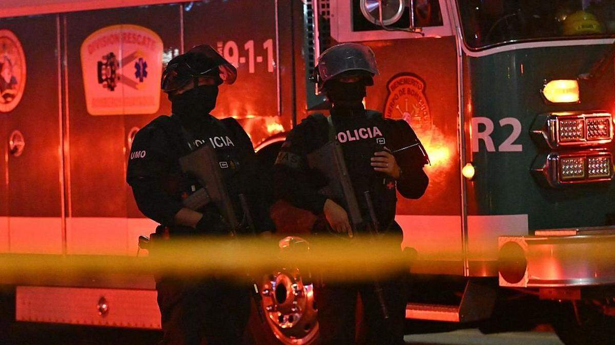 Police officers stand guard at the crime scene where a suspected car bomb exploded in front of a shopping center in the north of Guayaquil, Ecuador on October 14, 2025. One person died and several were injured after an explosion on Tuesday in a busy shopping area of the Ecuadorian port of Guayaquil, which was left in chaos, according to images released by local authorities. (Photo by Marcos Pin / AFP) (Photo by MARCOS PIN/AFP via Getty Images)