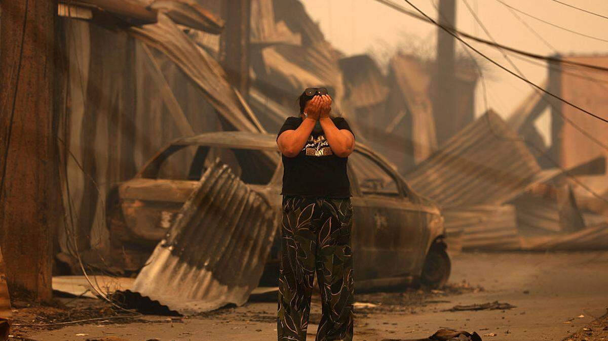 Una residente llora tras ver los restos de su casa y auto que fueron destruidos por un incendio en Concepción, en el sur de Chile, el domingo 18 de enero de 2026.