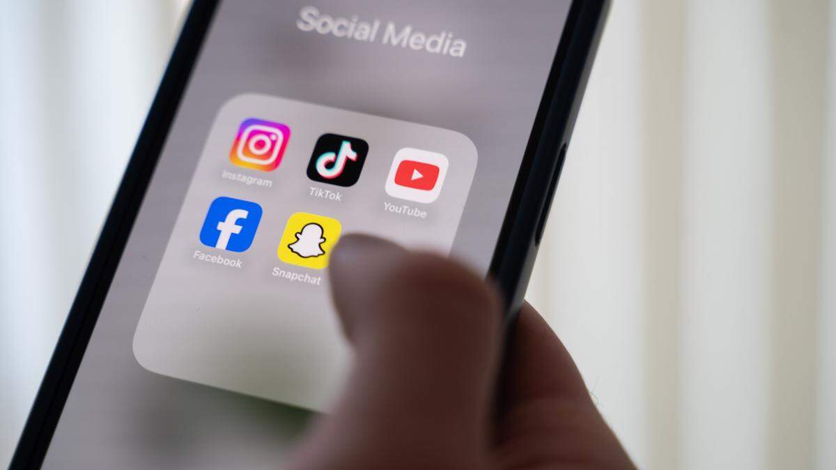 Una mujer sostiene un teléfono inteligente con varias aplicaciones de redes sociales en la pantalla.