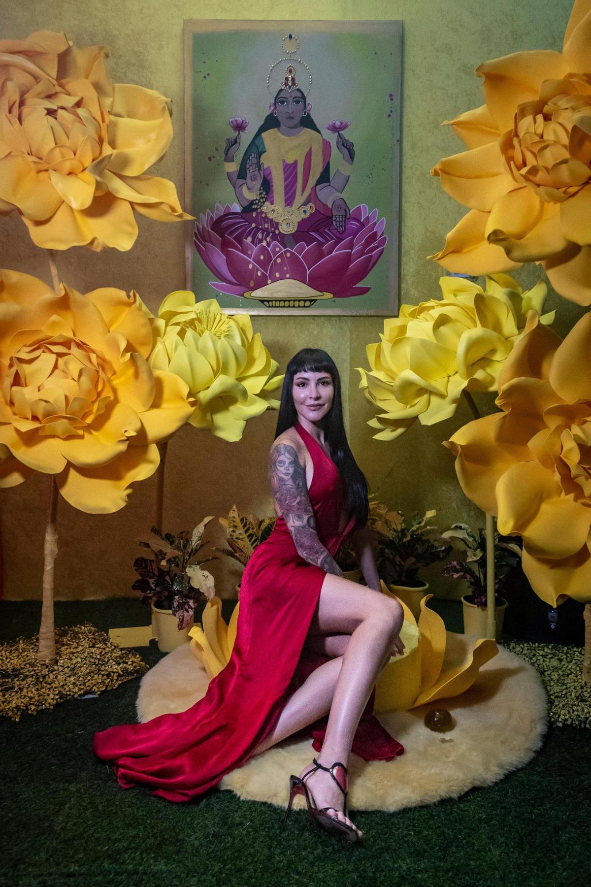 Miami, Florida, October 6, 2022 - Camimi Palomeque, an artist from Ecuador, sits in front of one of her paintings on display at the Chakras Garden exhibit. The Chakras Garden (Jardin de Chakras) is an immersive artistic experience developed by seven artists from different parts of the world, creating a unique work of art that represents the seven main chakras, through different spaces converted into a garden of colors, shapes and textures.