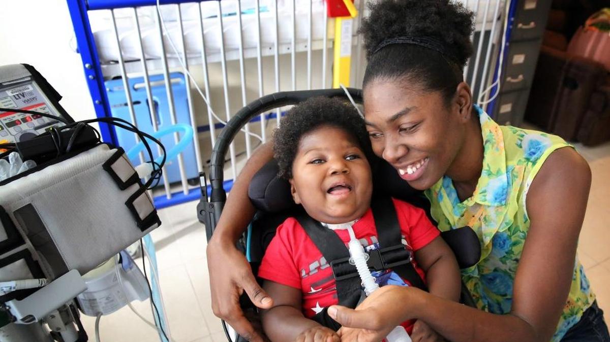 Antoinise Augustine, con su hijo de 17 meses, Samuel, en su estudio de North Miami. Samuel nació prematuramente con microcefalia. Samuel permanece en un respirador y se alimenta a través de un tubo. La silla de ruedas para bebés que usa ya le queda pequeña, por lo que transportarlo se ha vuelto cada vez más difícil. La familia está pidiendo una silla de ruedas para niños pequeños que pudiera ayudarle algún día para ir a la escuela.