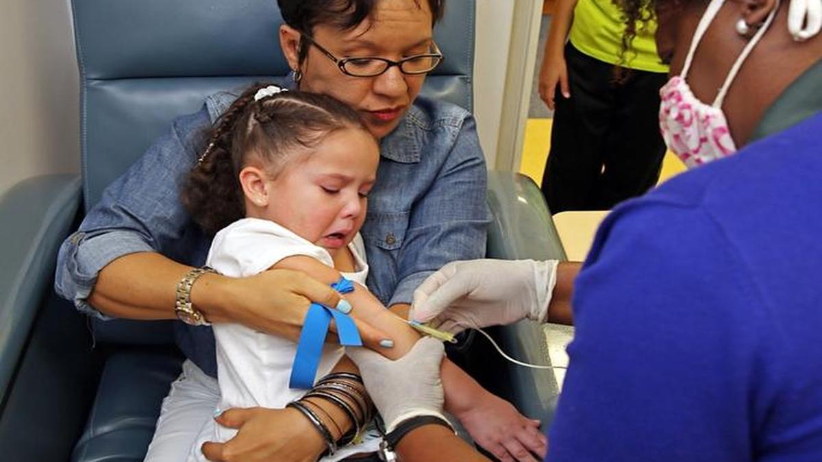 A Olivia Lolo, de 3 años, le sacan sangre para una prueba de diabetes ya que su hermano la padece. En la foto junto a su madre Stephanie Lolo y la investigadora de TrialNet, Paulette Smith.