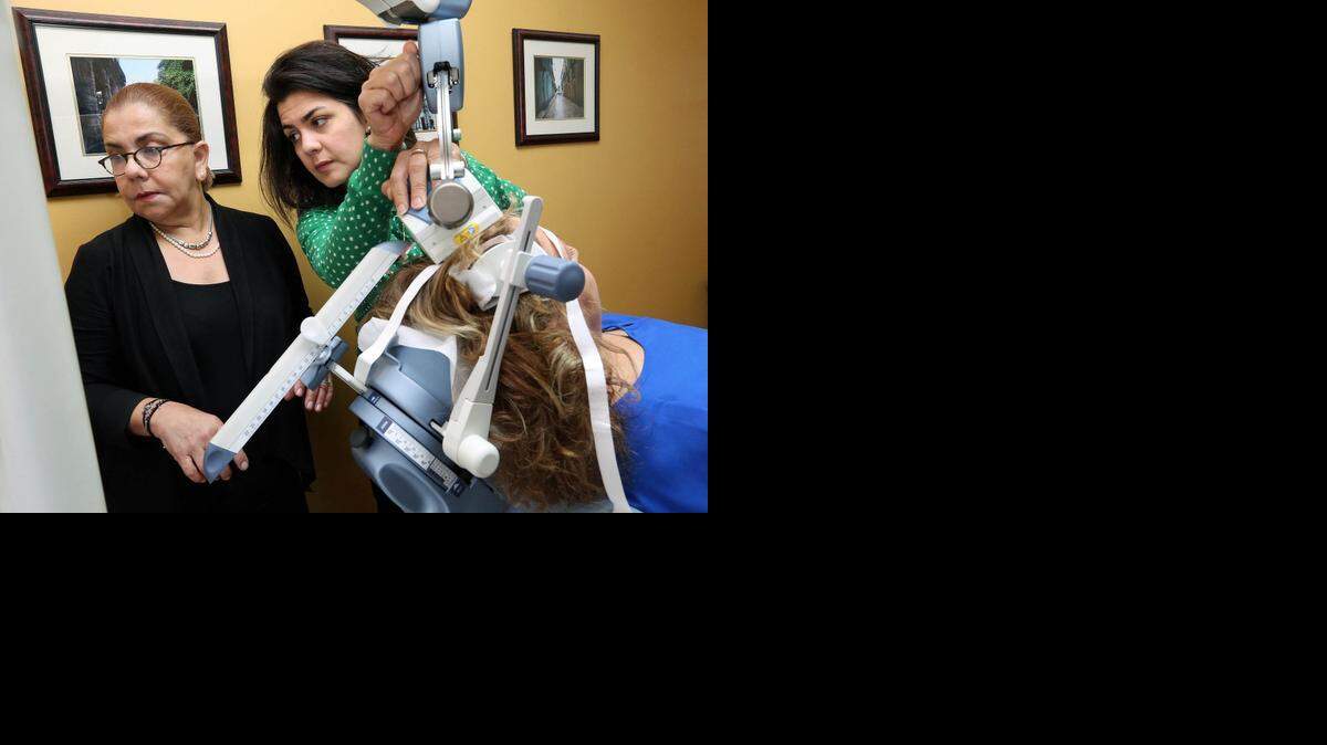 
La Dra. Arocha (izq.) y su asistente Diana Núñez (RN) calibran los impulsos magnéticos para tratar a la paciente.
