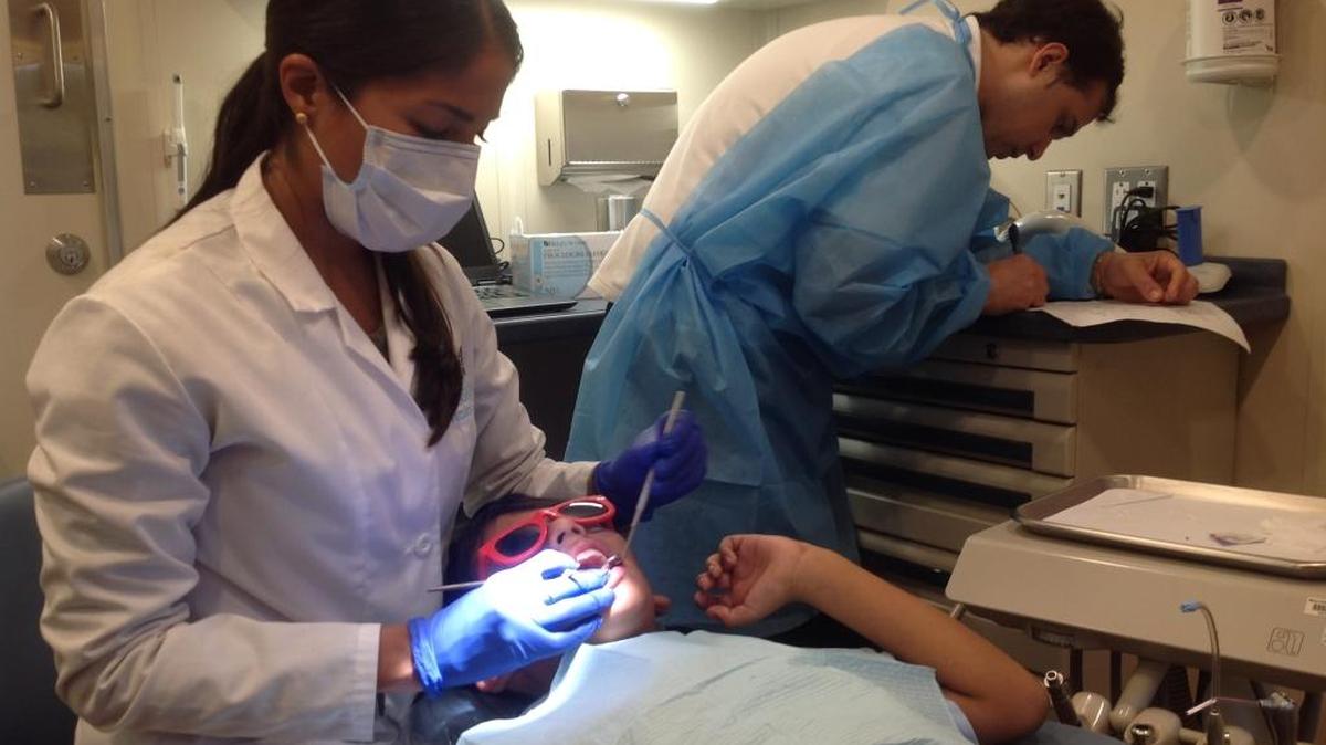 La dra. Melissa Meincken, supervisora de la clínica dental ambulante del Nicklaus Children's Hospital, atiende a Diego, de 8 años, mientras uno de los asistentes, Fabricio, toma nota.