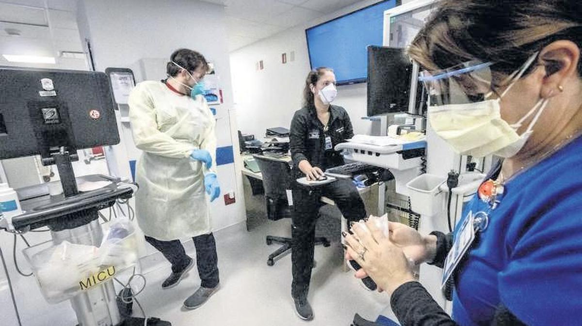 Nurse Alix Zacharski, right, sanitizes her hands as other doctors and nurses care for a patient in the Medical Intensive Care Unit for COVID-19 patients at Jackson Memorial Hospital in July during the surge caused by the delta variant. With the omicron variant spreading, Miami-Dade is requiring hospitals to resume daily reports on COVID patient counts and ICU bed availability.