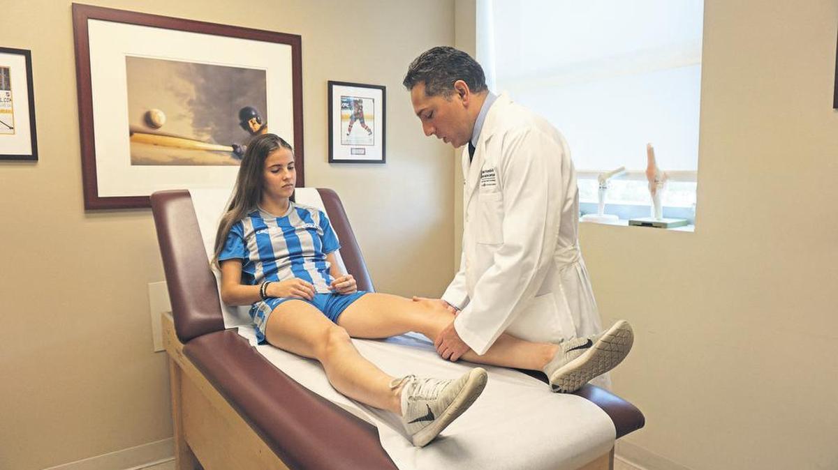 La deportista Karina Dourgery es examinada por Gautam Yagnik, cirujano ortopeda de Miami Orthopedics and Sports Medicine Institute. Abajo, el equipo de fútbol femenino de EEUU, campeón de la Copa Mundial 2019.