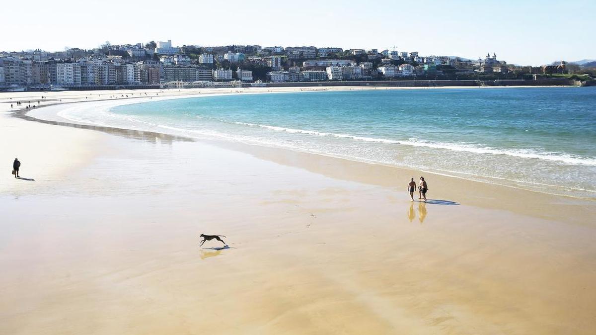 Unos paseantes pisan las aguas que destila la playa de La Concha de San Sebastián, una fría mañana de invierno.