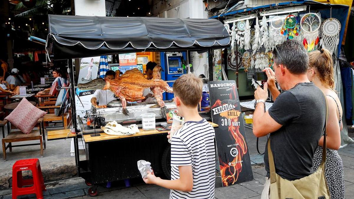 Varios turistas observan cómo asan un cocdrilo a la parrilla en el área de Khao San en Bangkok, Tailandia.