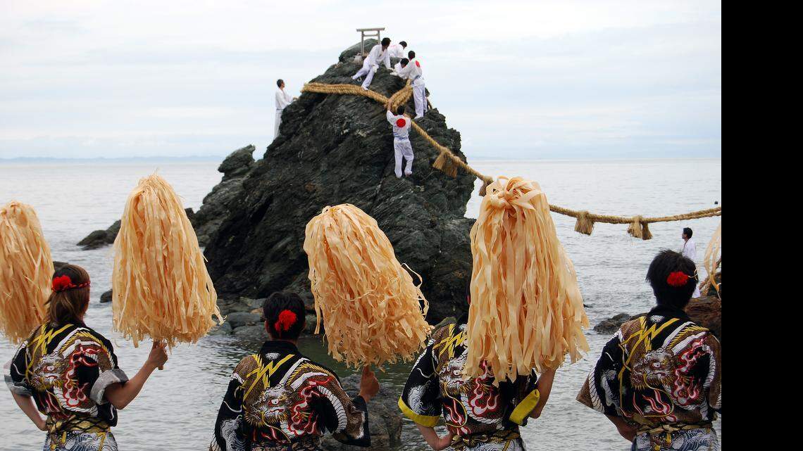 
Los ‘kiyari’, en primer plano, animan a los vecinos de Futami (Ise, prefectura de Mie, Japón), al fondo, durante la ceremonia del cambio de ‘shimenawa’ (soga hecha de paja de arroz) en las ‘rocas casadas’ (Meoto Iwa), situadas frente al Futami Okitama Jinja.
